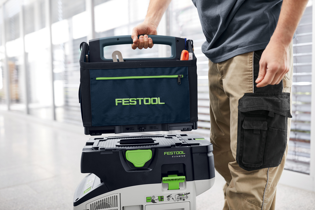 Person carrying a navy blue and black Festool storage bag on top of a modular tool chest for workshop organization