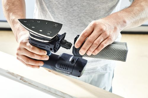 Person attaching dust collection attachment to cordless delta sander for home improvement tasks.