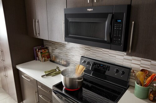 Modern kitchen with black Whirlpool over-the-range microwave and electric stove cooking boiling pasta on countertop