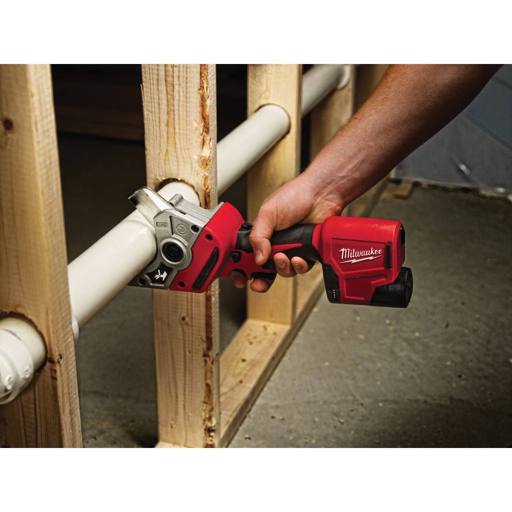 Red and black Milwaukee cordless plastic pipe shear cutting white plastic pipe in home improvement setting