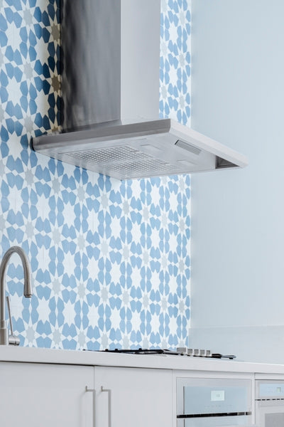 Stainless steel pyramid chimney wall hood installed above stove with blue floral tile backsplash in modern kitchen setting