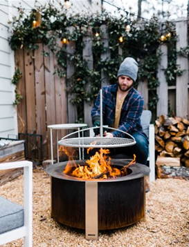 Outdoor fire pit grill with adjustable metal grate for cooking over wood fire in backyard setting
