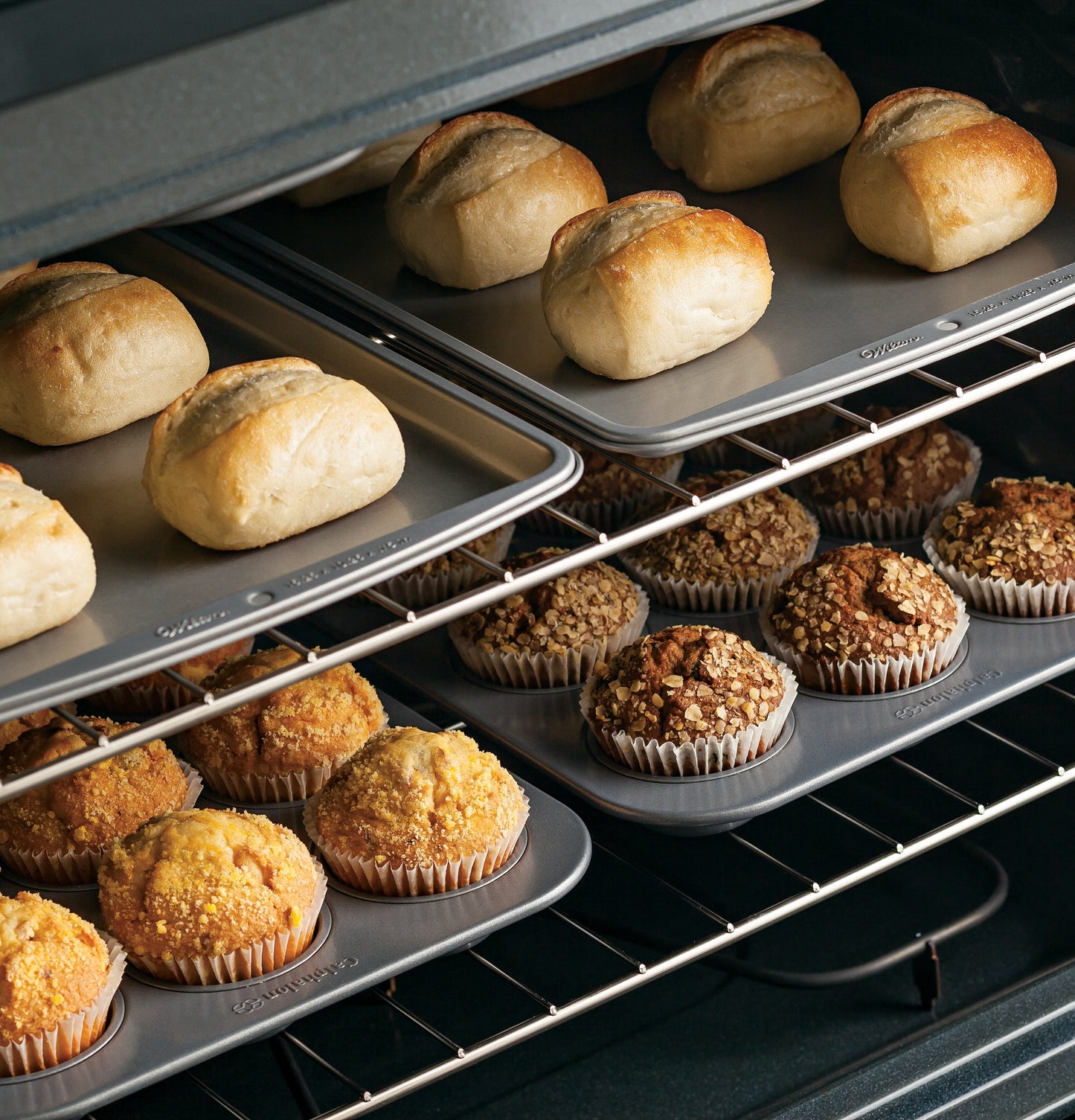 Freshly baked rolls and muffins on baking trays inside a modern oven of a free-standing electric range