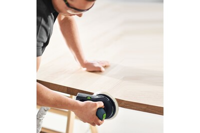 Person wearing safety glasses using a random orbit sander on a light wood surface for home improvement tasks