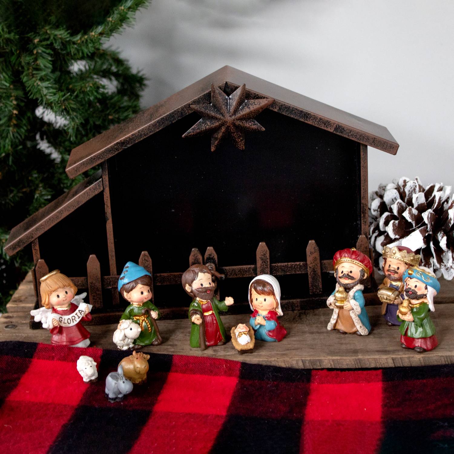Small colorful nativity figurines with metal creche and pinecone on red plaid for Christmas nativity scenes under $100
