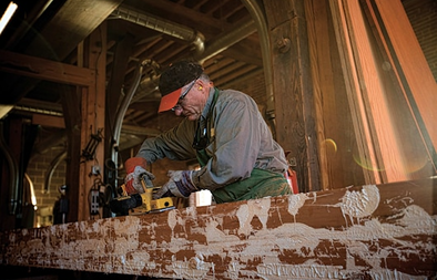 Man using a cordless brushless planer on a large wooden beam in a workshop for home improvement tasks