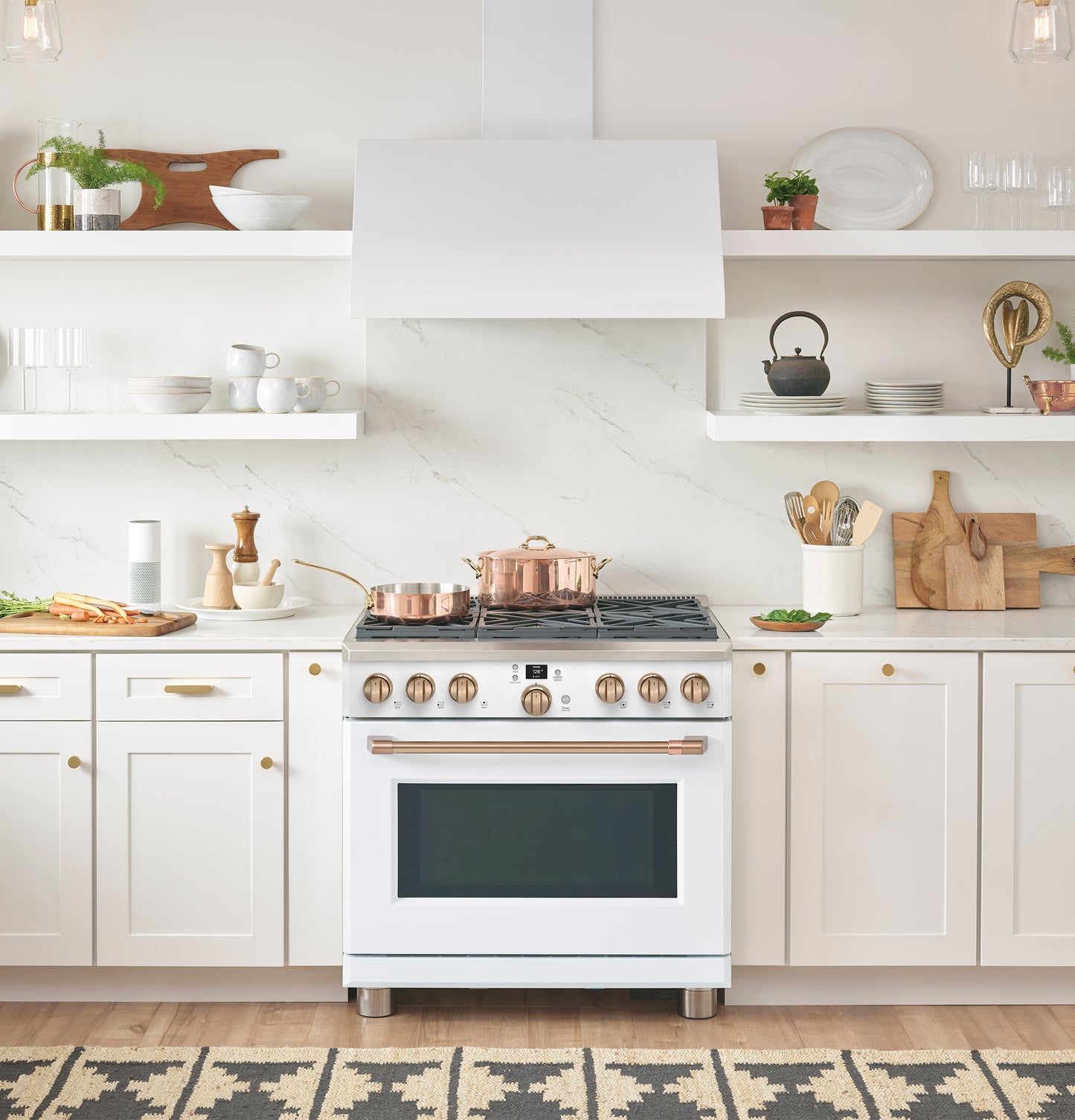 White modern wall-mounted range hood above gas stove with copper cookware in bright kitchen setting