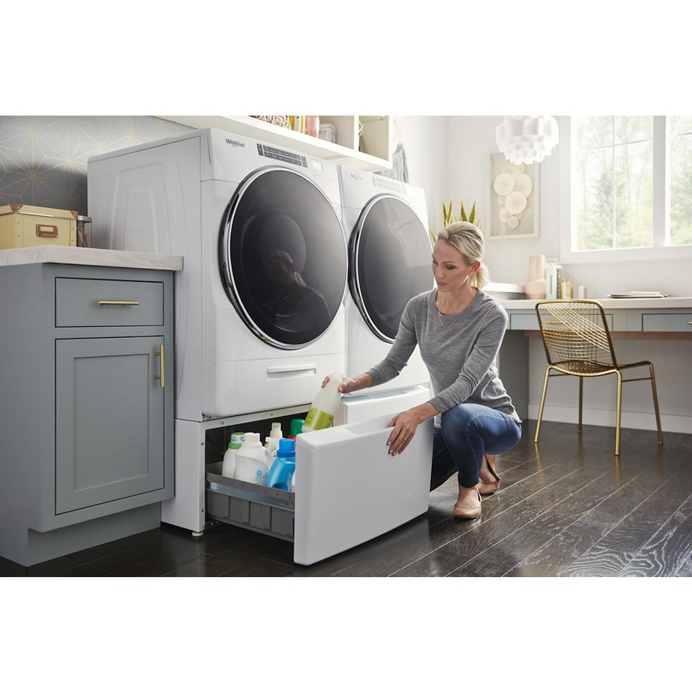 Woman kneeling by white front load dryer pedestal drawer organizing laundry detergent in bright laundry room with natural light