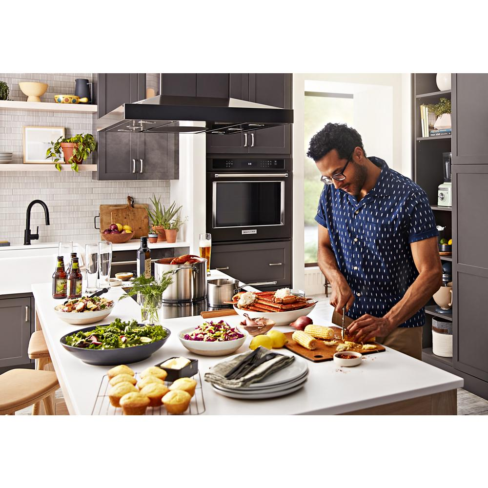 Man preparing food on a kitchen island surrounded by fresh ingredients and modern dark gray cabinetry appliances