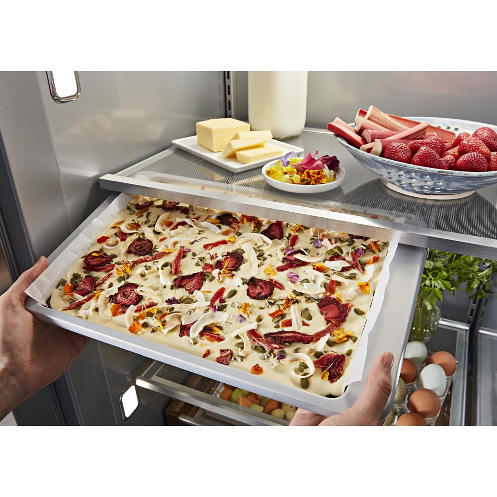 Hands sliding a flat pan with prepared food into an adjustable shelf inside a built-in KitchenAid side-by-side refrigerator