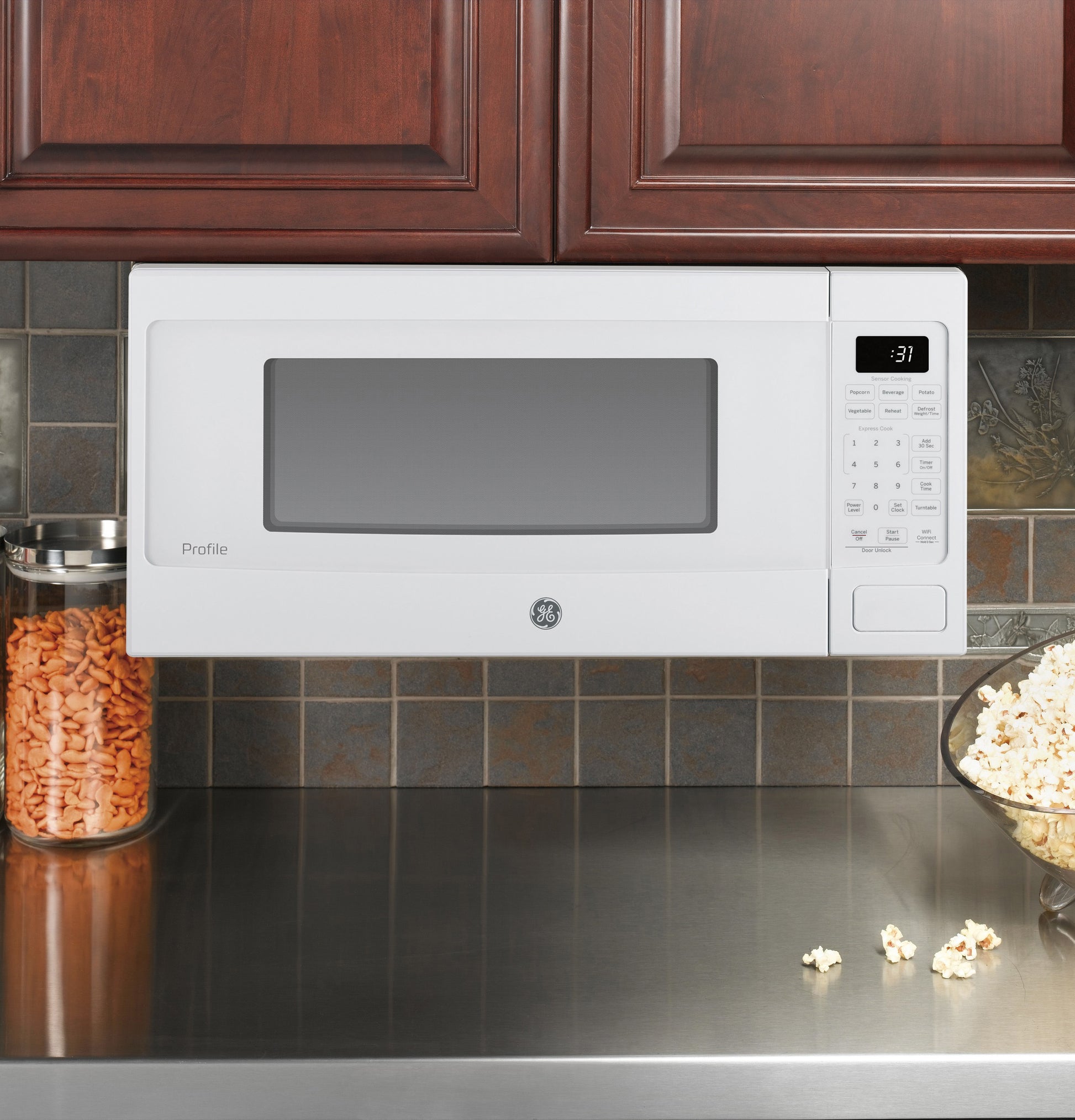 White GE Profile microwave oven mounted under wooden cabinets with digital control panel in kitchen setting