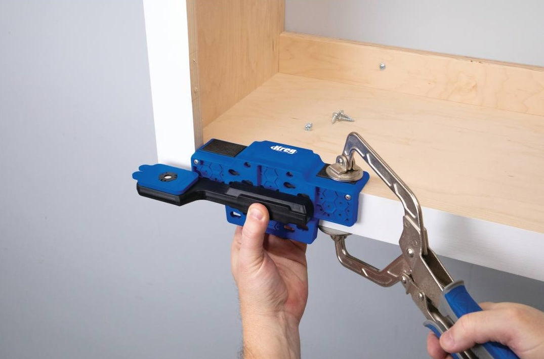 Blue and black cabinet door mounting jig held with locking pliers for precise woodworking tool setup in home improvement