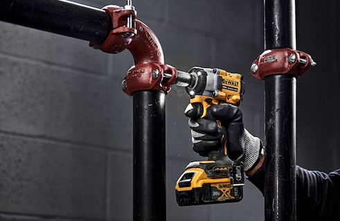 Gloved hand operating yellow and black cordless impact wrench on black metal pipe for home improvement tasks