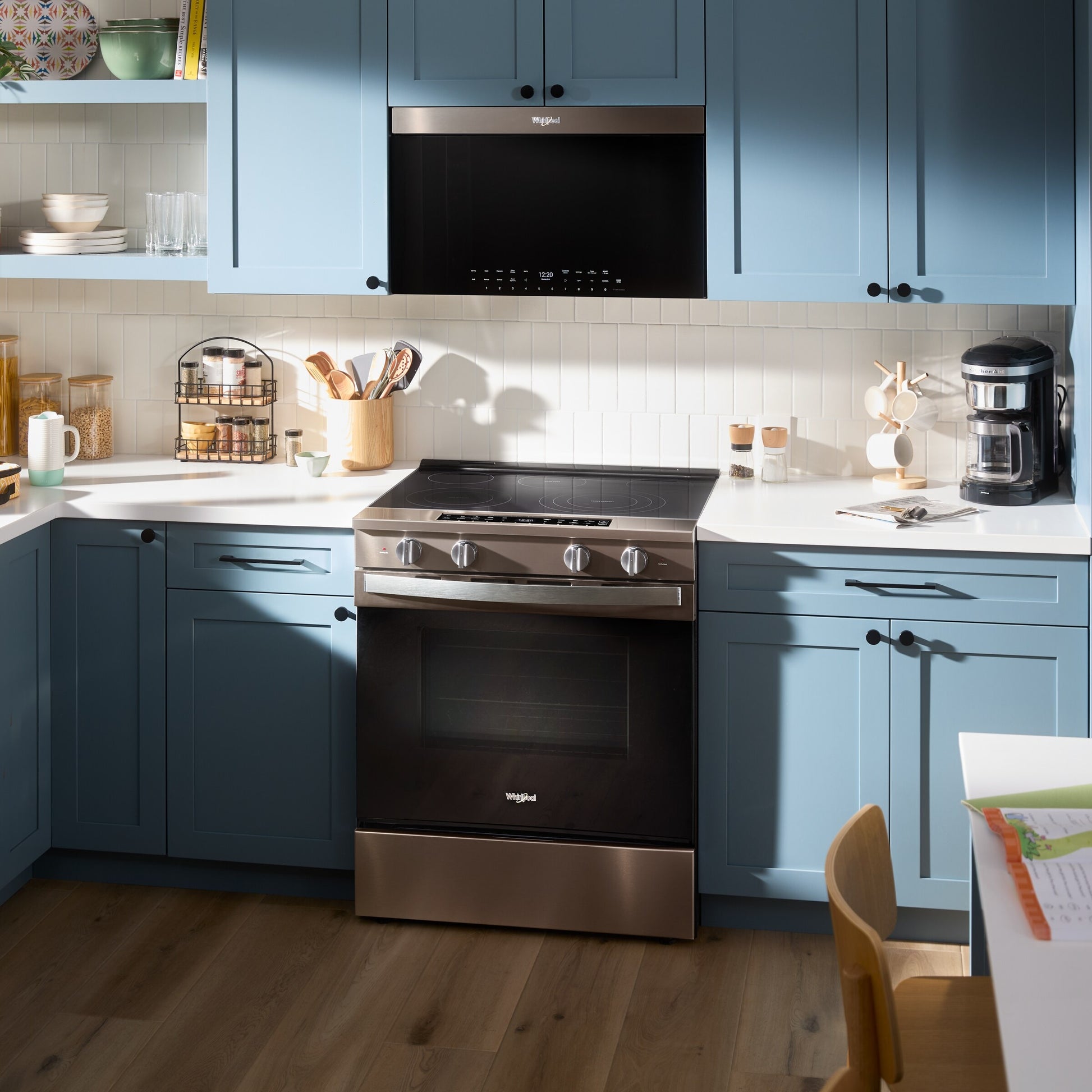 Black Whirlpool microwave with touch controls mounted above stainless steel electric range in kitchen setting with blue cabinets