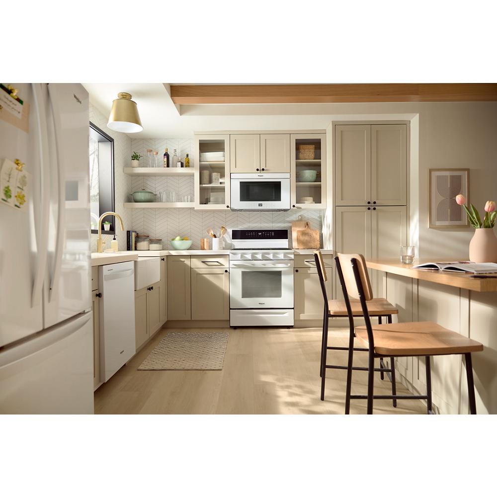 Bright kitchen with beige cabinets, white smart gas range, microwave, and breakfast bar with wood stools and flowers