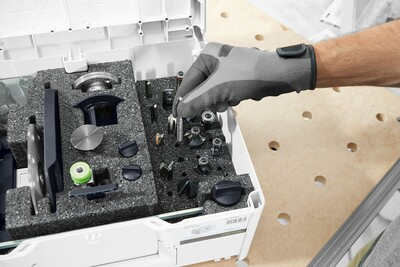 Gloved hand organizing precision routing accessories in a foam-lined organizer for woodworking tool storage and home improvement.