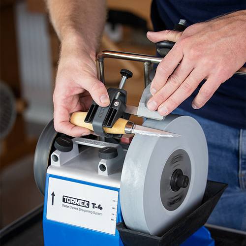 Person sharpening a knife using a Tormek SVM-00 small knife holder jig on a water-cooled sharpening wheel for tools and home improvement