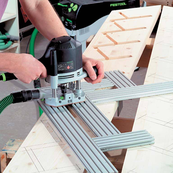 Hands guiding a Festool router with guide rails on angled wooden boards for precise woodworking and home improvement tasks