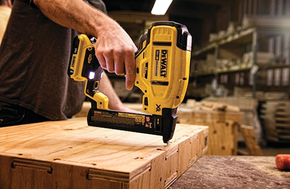 Person using yellow DEWALT cordless narrow crown stapler on wooden project in workshop for home improvement tasks