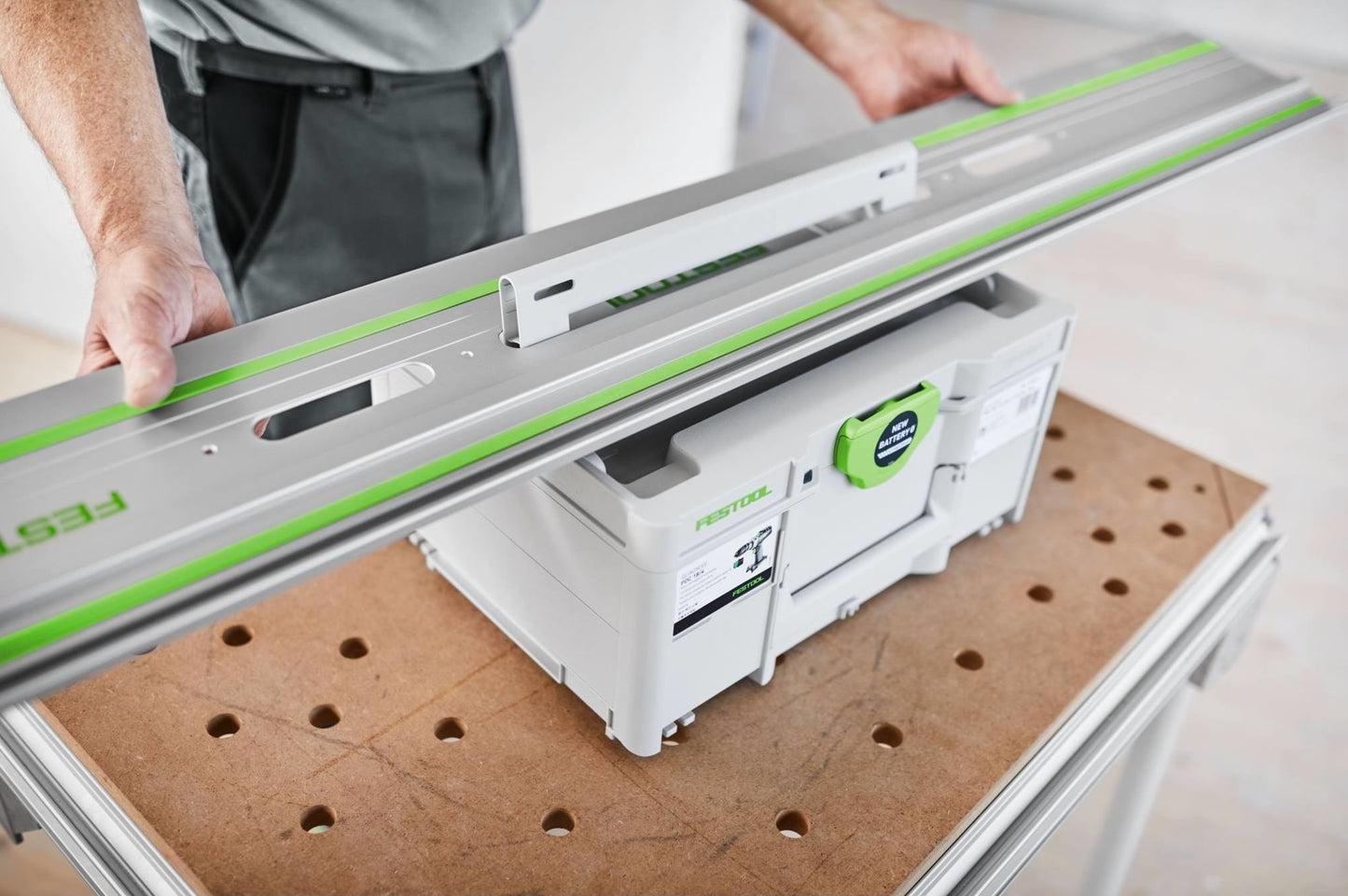 Precision guide rail with green accents being positioned over a Festool storage box on a woodworking bench