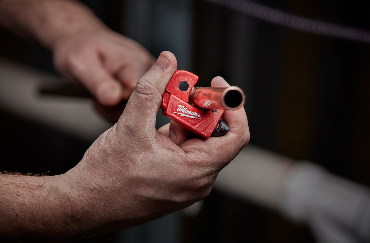 Hands holding a red Milwaukee mini cutter trimming copper tubing for tools and home improvement projects
