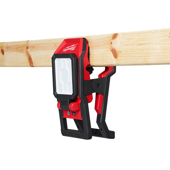 Red and black Milwaukee clamp light attached to wood beam with adjustable LED flood panel for versatile work lighting