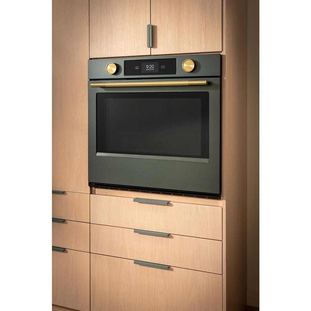 Juniper smart electric wall oven with gold-tone knobs and handle, LED display integrated into light wood cabinetry in KitchenAid collection