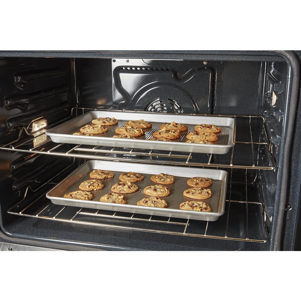 Two metal baking sheets with chocolate chip cookies baking inside a kitchen wall oven from appliances collection