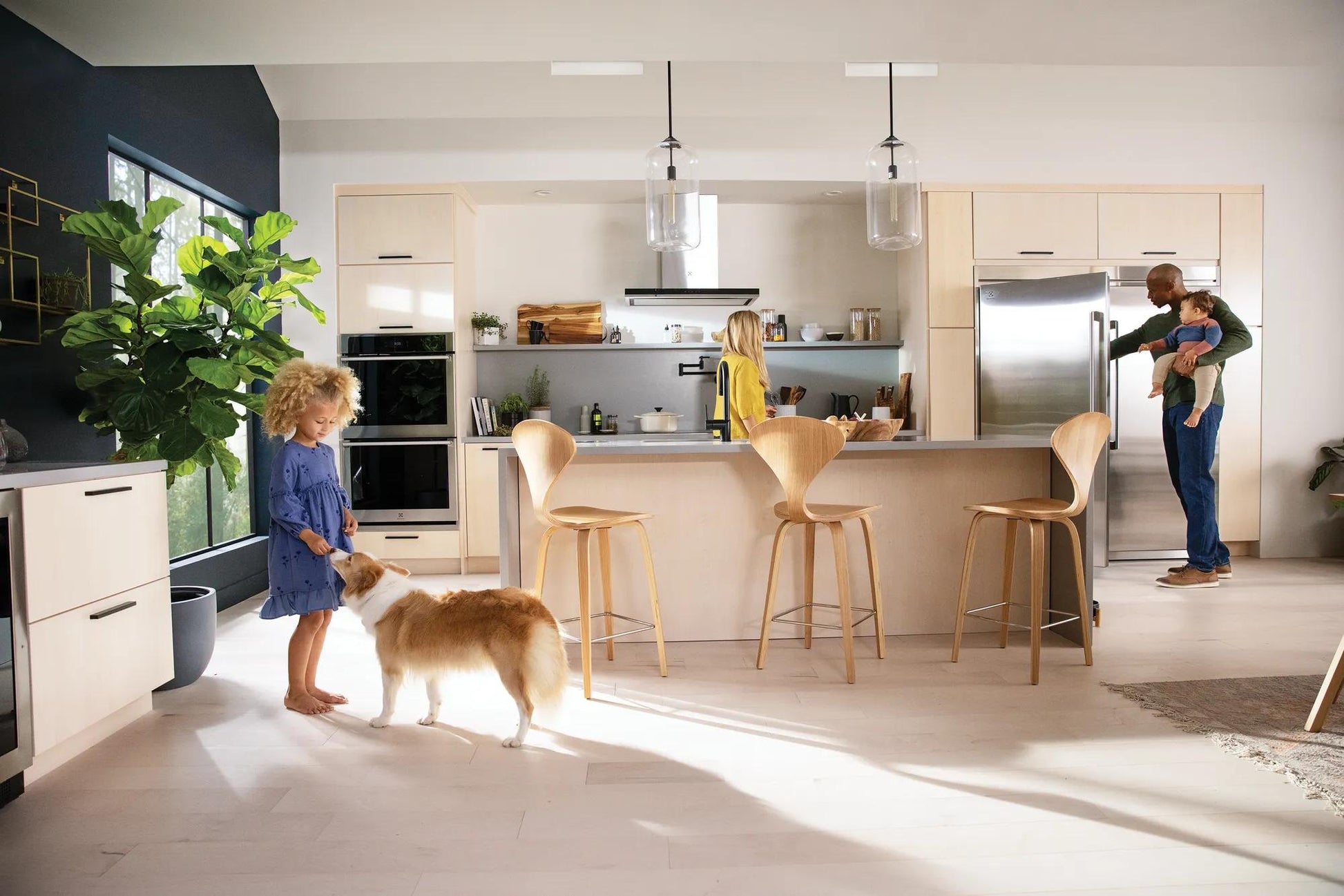 Modern kitchen with stainless steel freezer, light wood cabinetry, island seating, and family interacting in Appliances collection