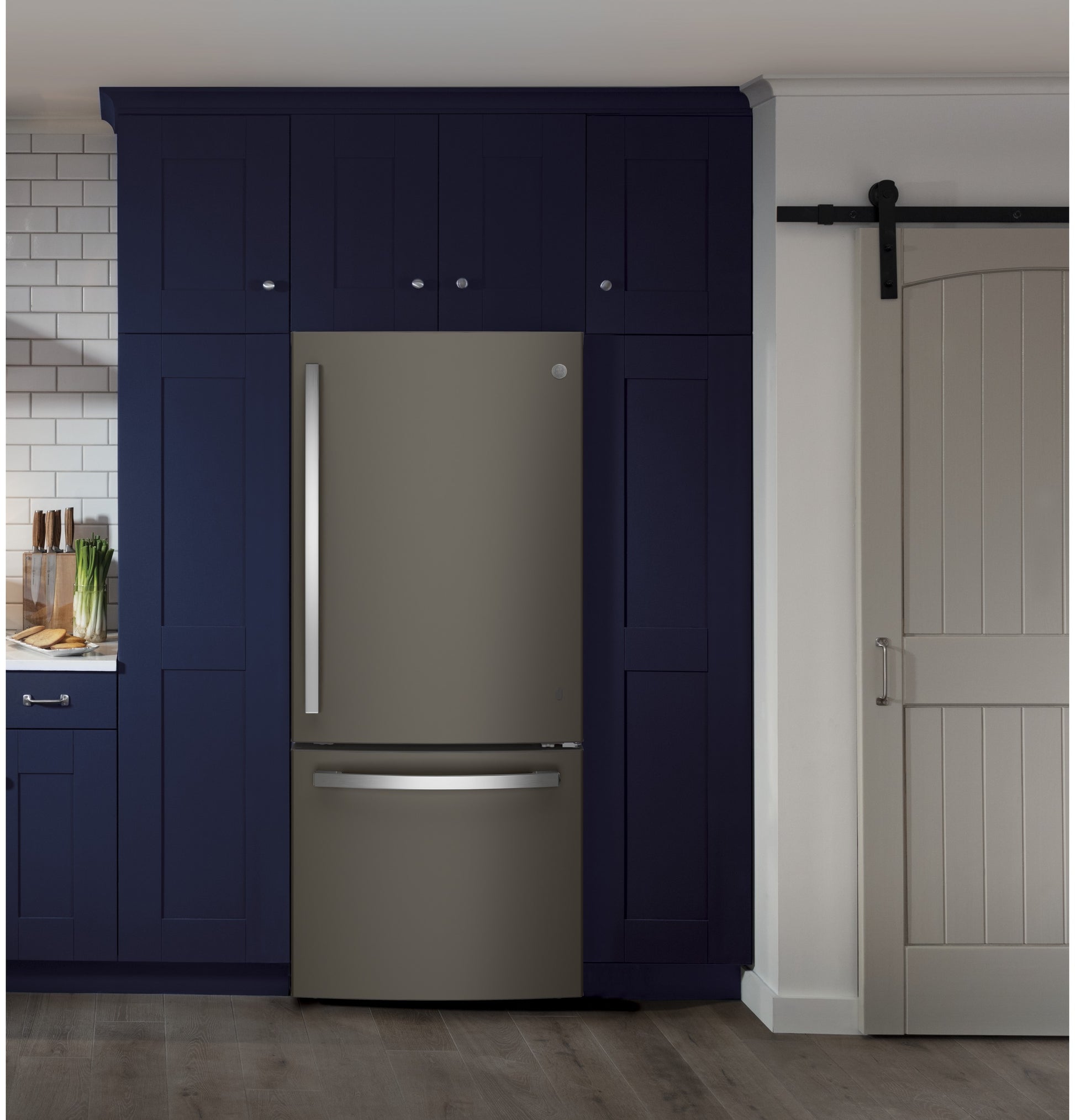 Built-in matte stainless steel bottom-freezer refrigerator integrated into navy blue kitchen cabinetry with sliding barn door nearby