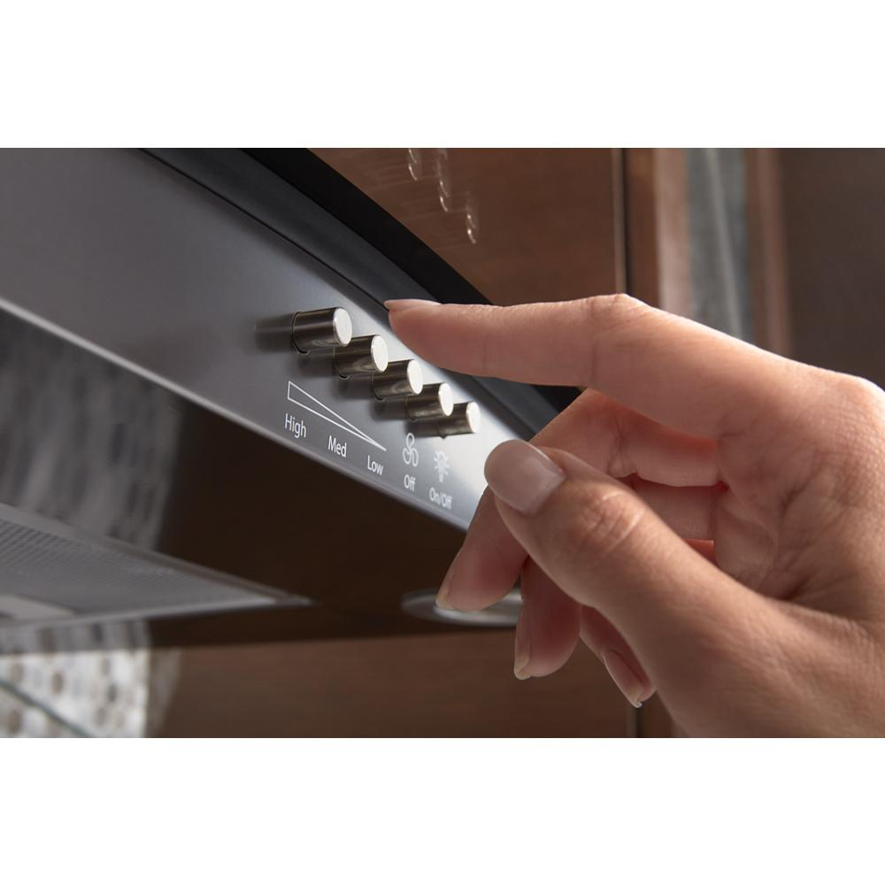 Close-up of hand adjusting fan speed controls on a concave glass wall mount range hood from kitchen appliances collection