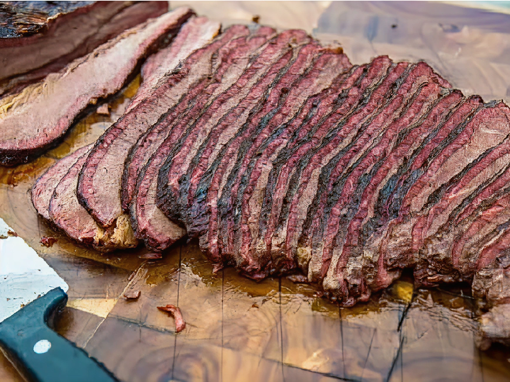 Close-up of sliced smoked beef brisket arranged on a wooden cutting board, showing a dark bark and pink smoke ring.
