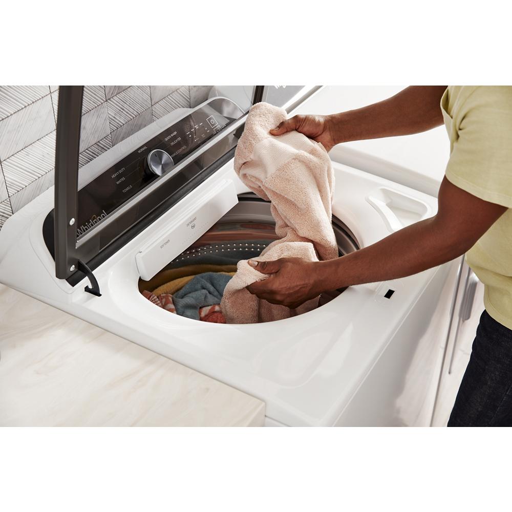 Person loading towels into a white top-loading washer with open lid in a modern laundry room setting