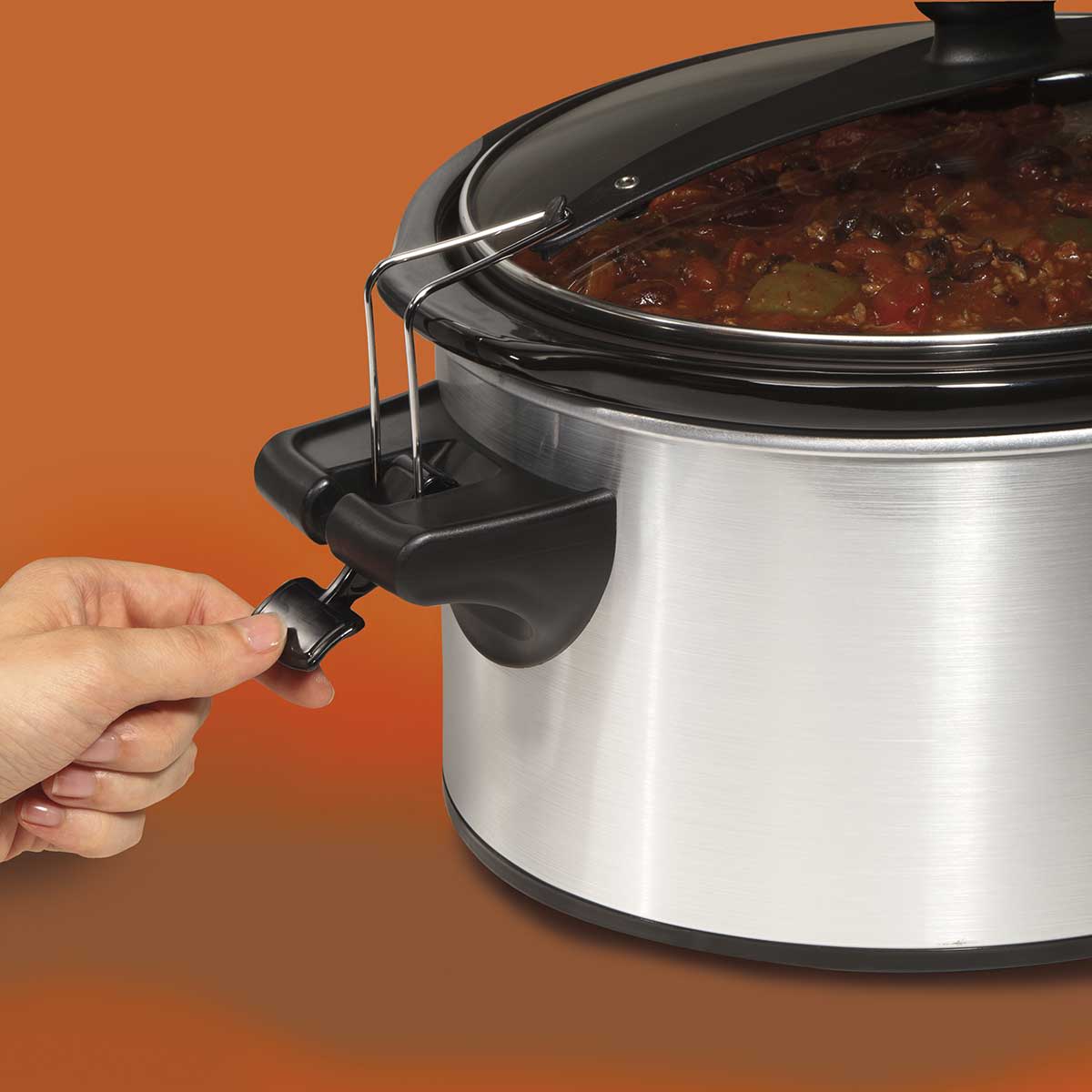 Hand securing clear locking lid on stainless steel slow cooker in small kitchen appliances category