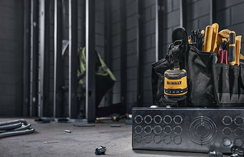 Yellow and black rechargeable mini Bluetooth speaker resting next to a tool bag in a workshop setting for home improvement
