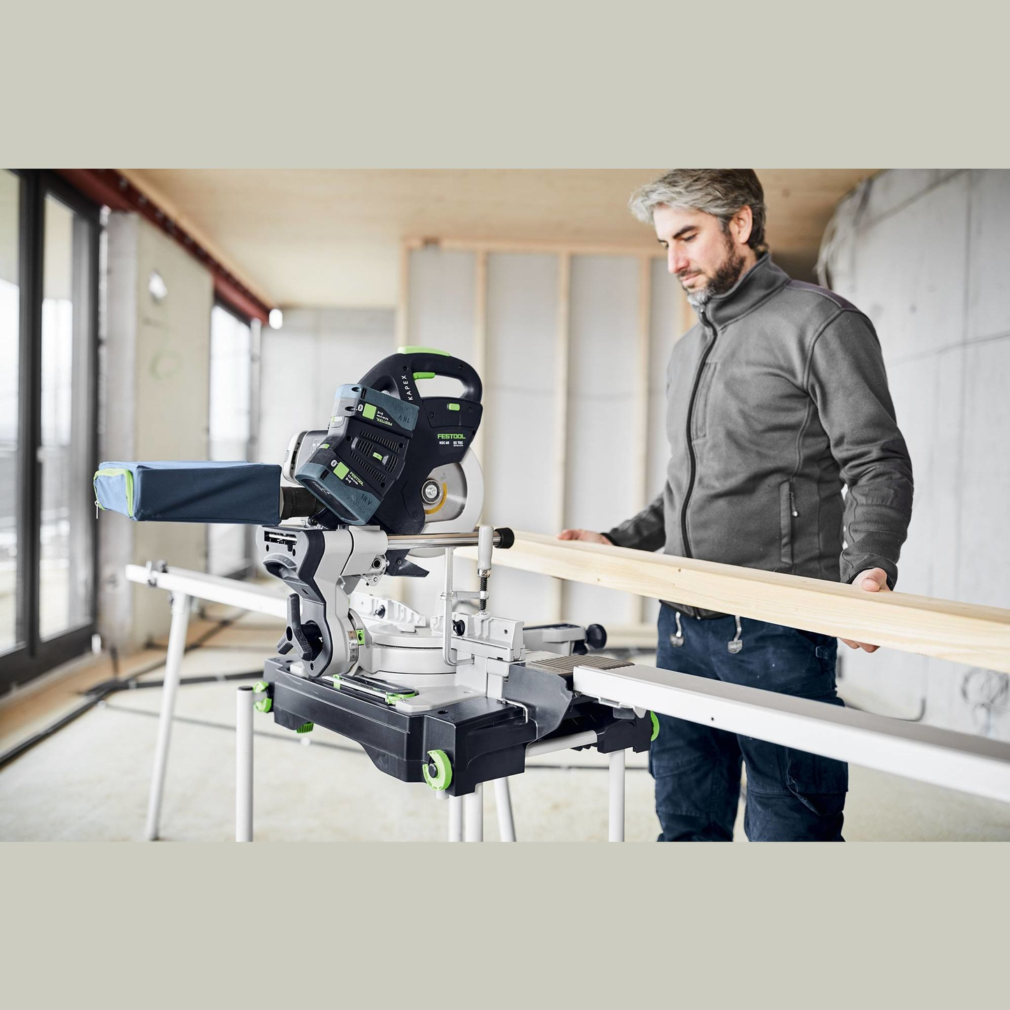 Man using cordless compound miter saw on woodworking project in bright workshop with natural light