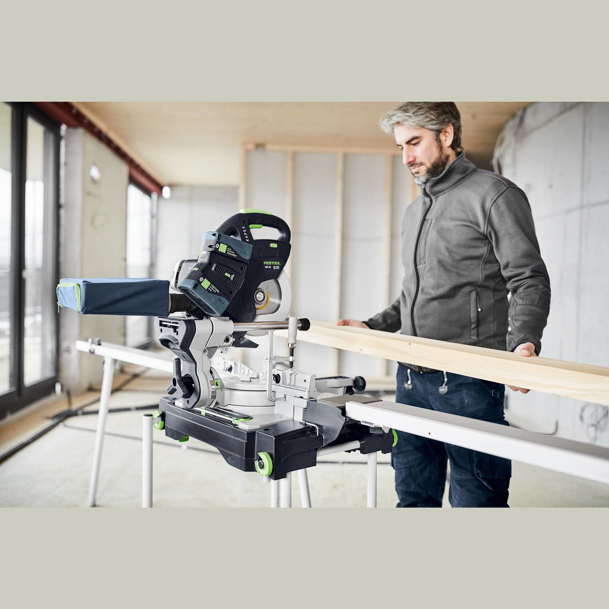 Man using cordless compound miter saw on woodworking project in bright workshop with natural light