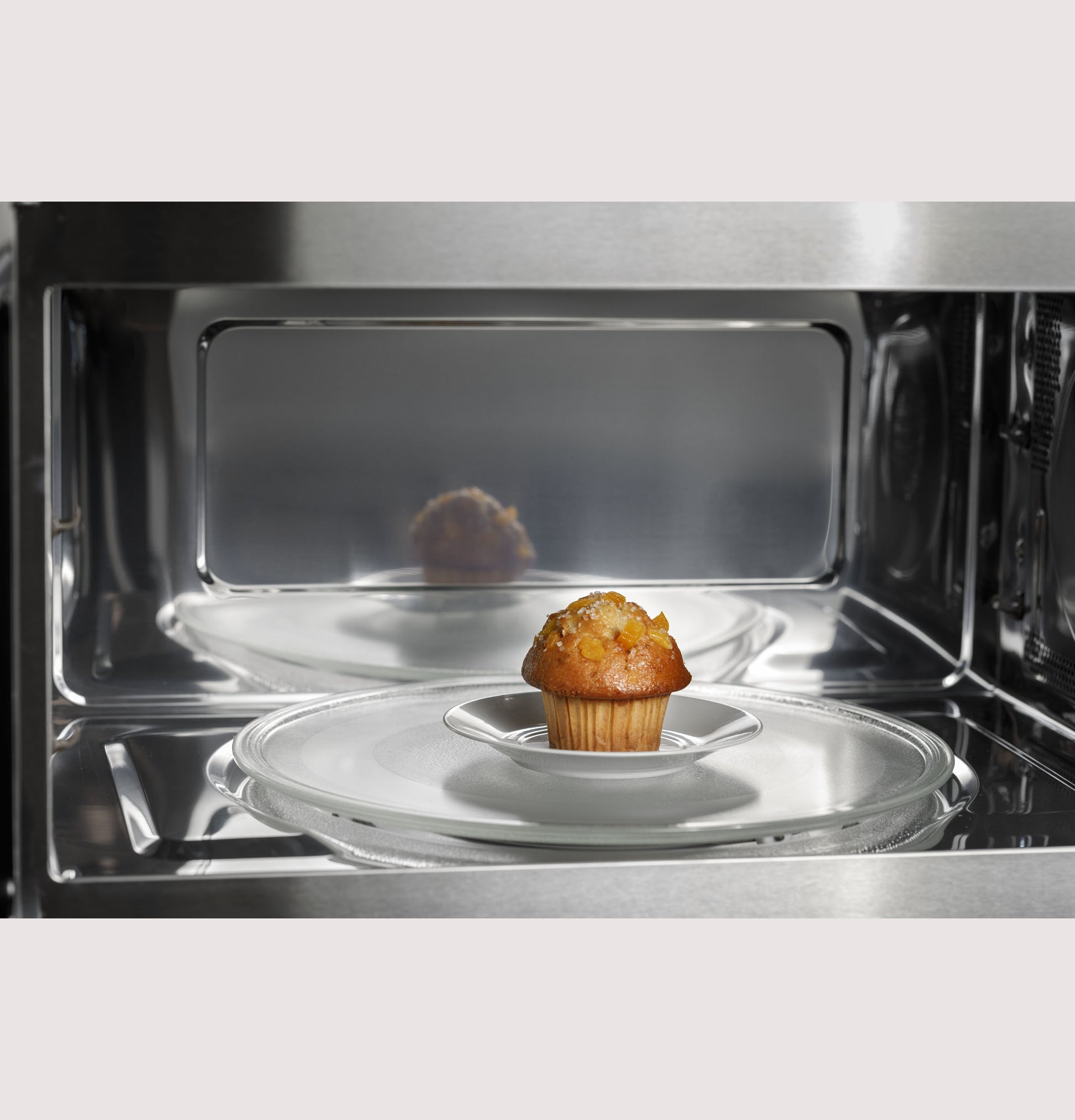 Interior of convection microwave oven with glass turntable and a single muffin inside in kitchen appliances setting