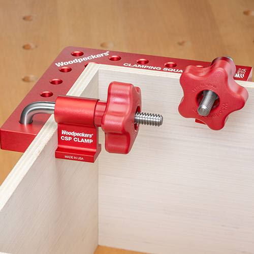 Red aluminum clamp with ergonomic knob securing wood pieces at a right angle for precise woodworking assembly.