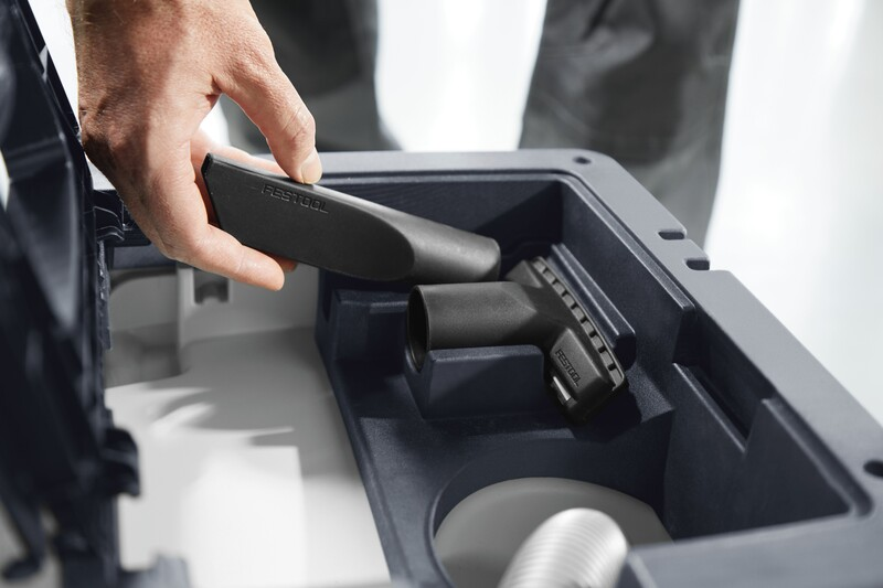 Hand holding black crevice nozzle being placed into storage compartment of Festool vacuum accessory case for dust management.