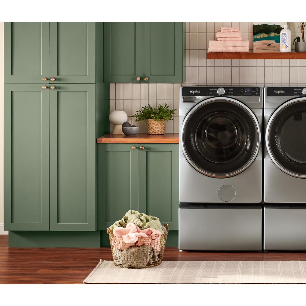 Silver front load washer and dryer set next to green cabinetry with laundry basket on rug in laundry room