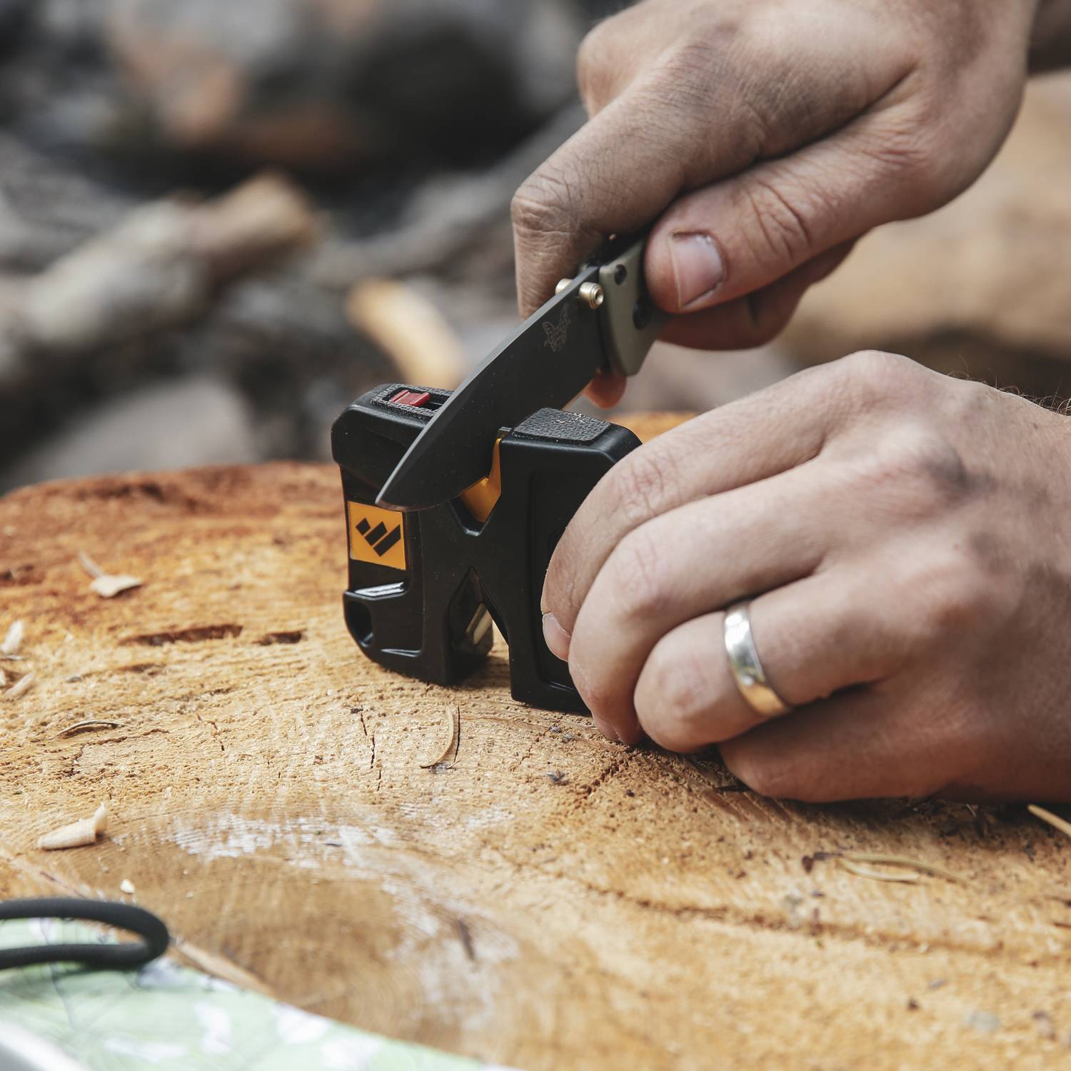 Hands using a black and yellow pivot knife sharpener on folding knife on wood surface for tools maintenance