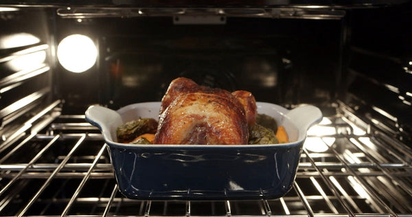 Roast chicken cooking alongside vegetables inside stainless steel Thermador double wall oven from kitchen appliances collection