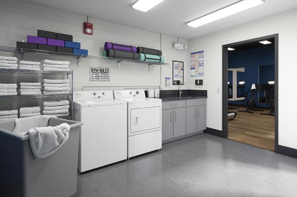 White commercial gas dryer with matching washer in a clean laundry room next to gray cabinets and folded towels