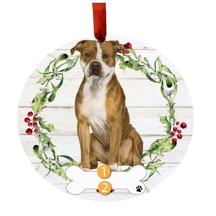 Round Christmas ornament featuring a brown and white pit bull inside a green wreath with red berries and white accents