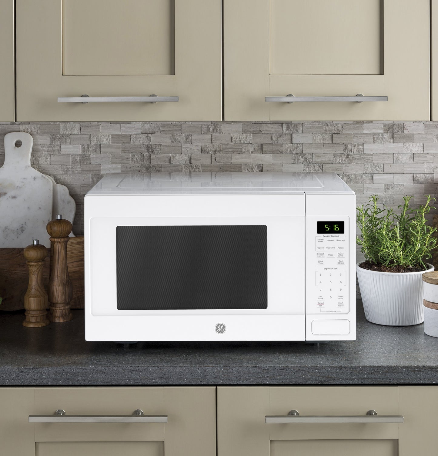 White countertop microwave oven with digital display and control panel set on kitchen counter with stone backsplash and olive cabinets
