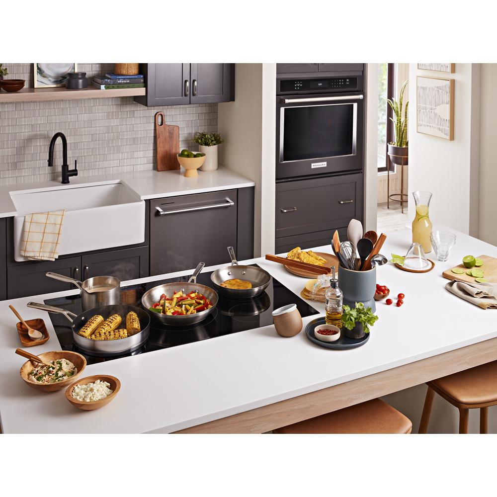 Modern kitchen with a 36-inch black 5-element sensor induction cooktop and various cookware from KitchenAid appliances collection