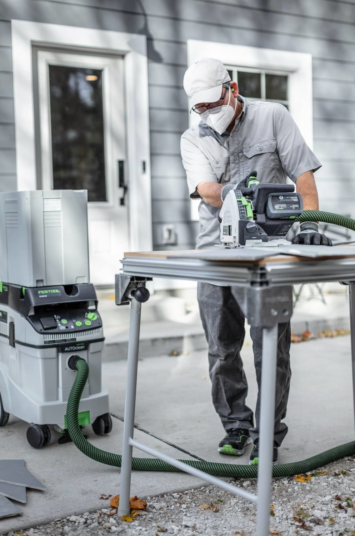 Person using Festool cordless track saw with connected dust extractor outdoors on portable workbench