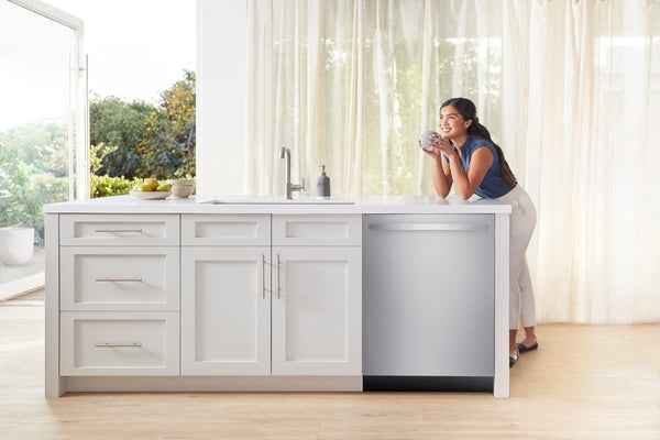 Modern kitchen island with stainless steel 24-inch dishwasher and woman enjoying a drink by the window