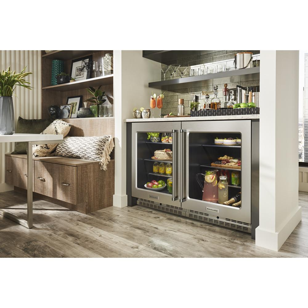 Dual-door undercounter refrigerator with glass doors, metallic accents, stocked with drinks and snacks in modern kitchen setting